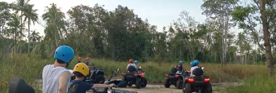 Group of people riding ATVs on a sandy trail surrounded by trees.