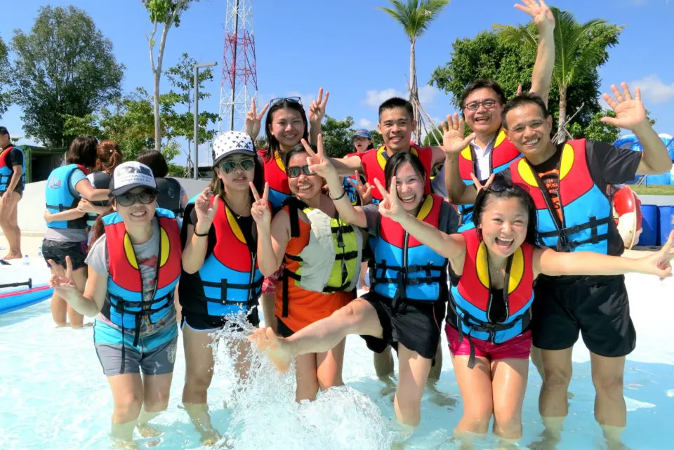 Group of cheerful people in life vests posing in water, smiling and making peace signs