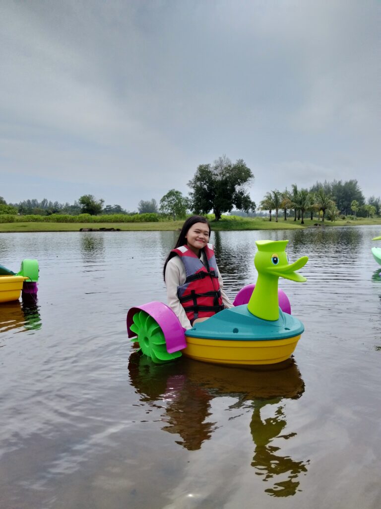 Young girl smiling and paddling a colorful yellow and purple duck-shaped pedal boat on a