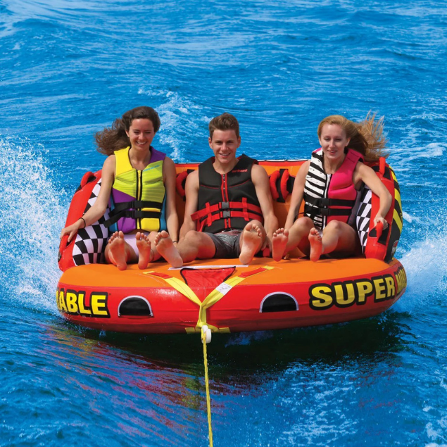 Four smiling people enjoying a ride on a bright yellow and orange Super Sofa towable