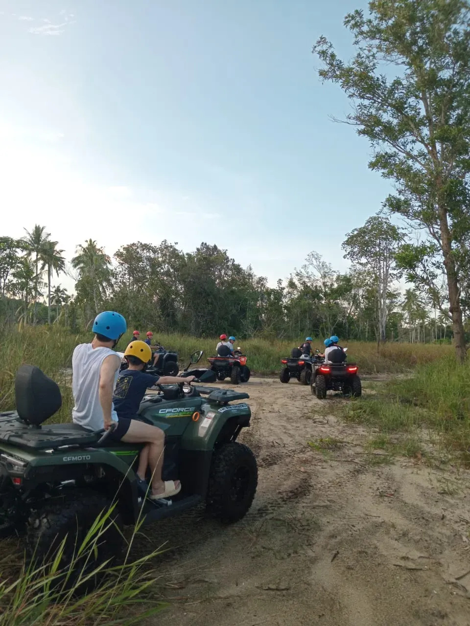 Group of people riding ATVs on a sandy trail surrounded by trees